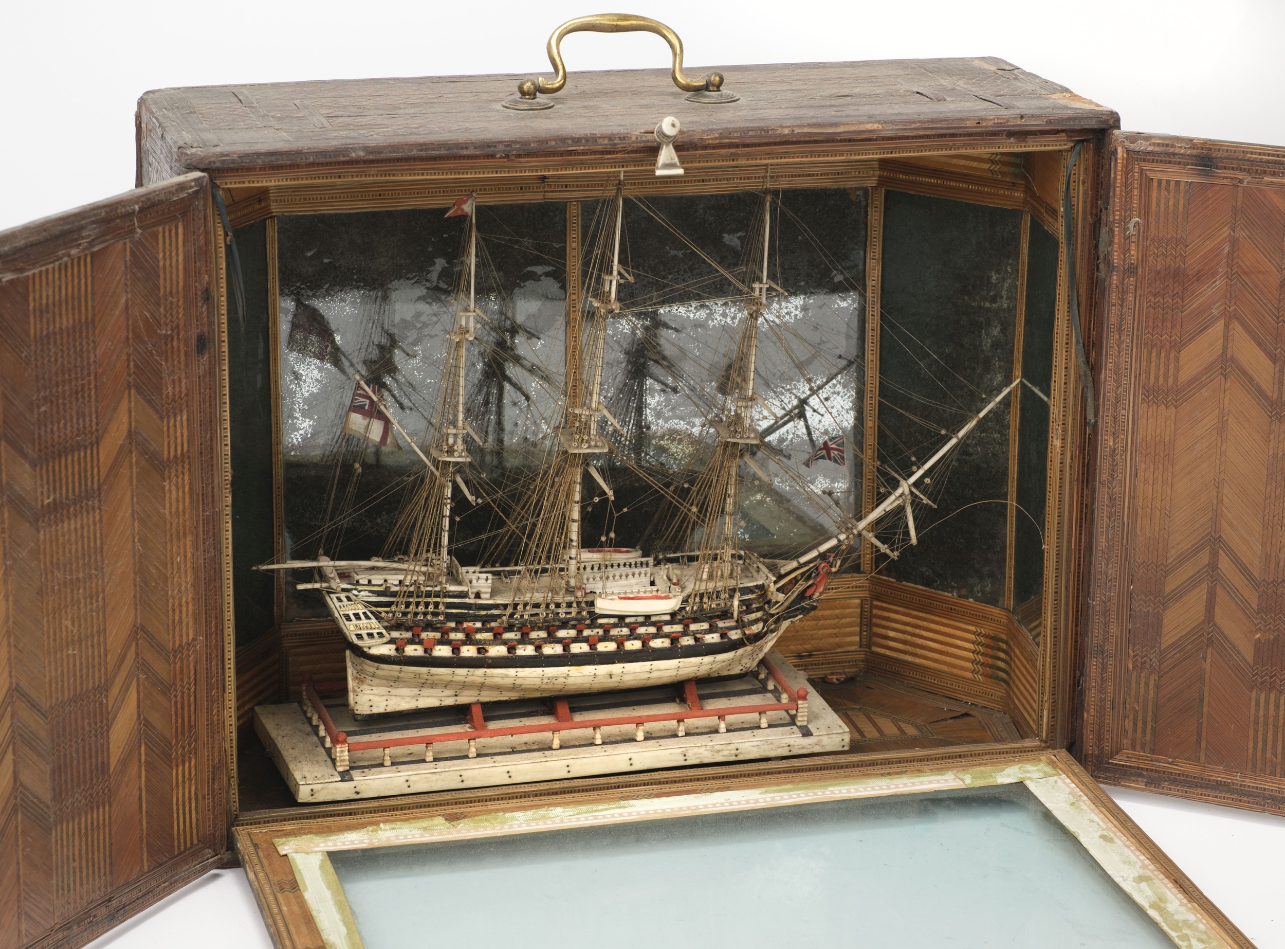 A bone model ship, displayed within a straw-work case.