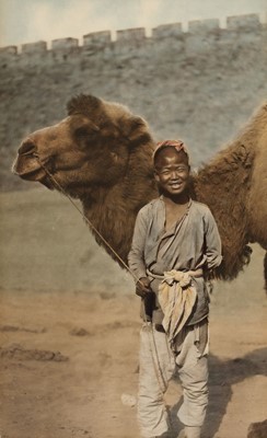 Lot 316 - China. A smiling boy holding the tether of his camel, hand-coloured carbon print, China, 1920s