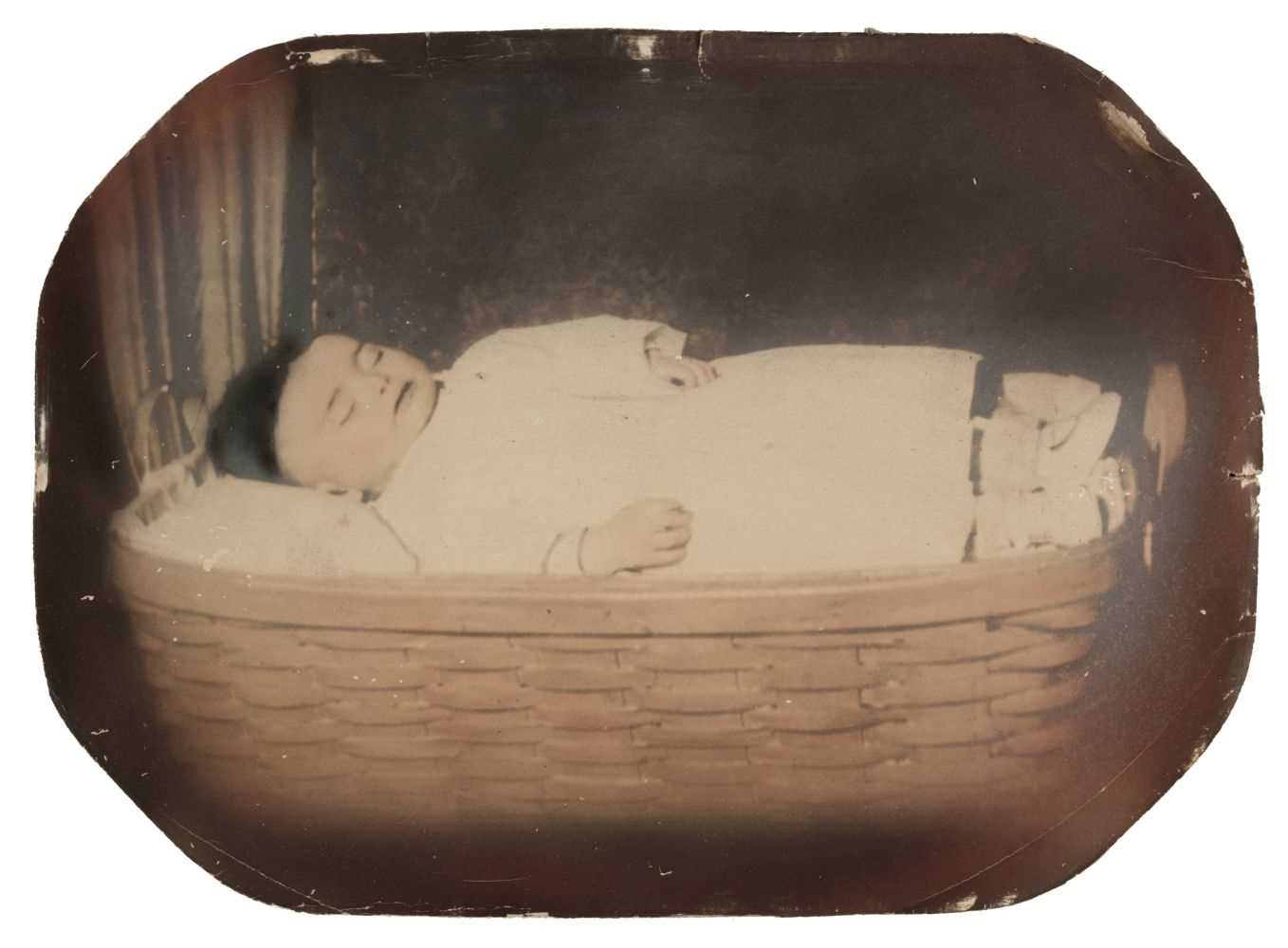 Lot 24 - Post-mortem of a child. A full-length portrait of a young child lying in a wicker basket, c. 1880s