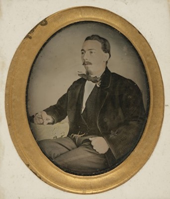 Lot 118 - Ambrotype. A hand-tinted ambrotype of a man seated at a table smoking, probably Spanish, c. 1870s